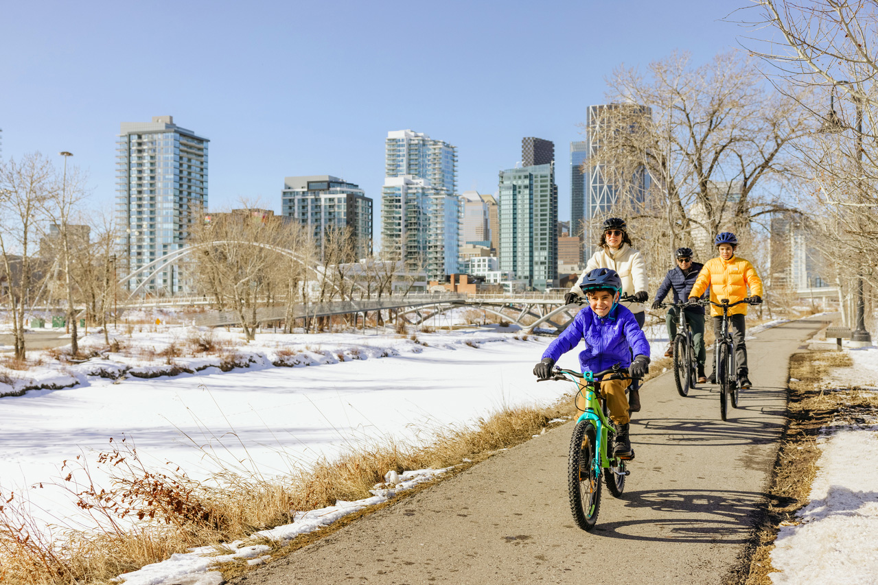 A family bikes on the trails with views of the Calgary skyline in the background