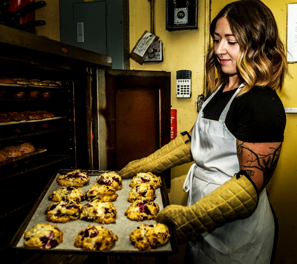 A baker at Purple Perk puts a tray of scones, fresh from the oven, onto a cooling rack for brunch