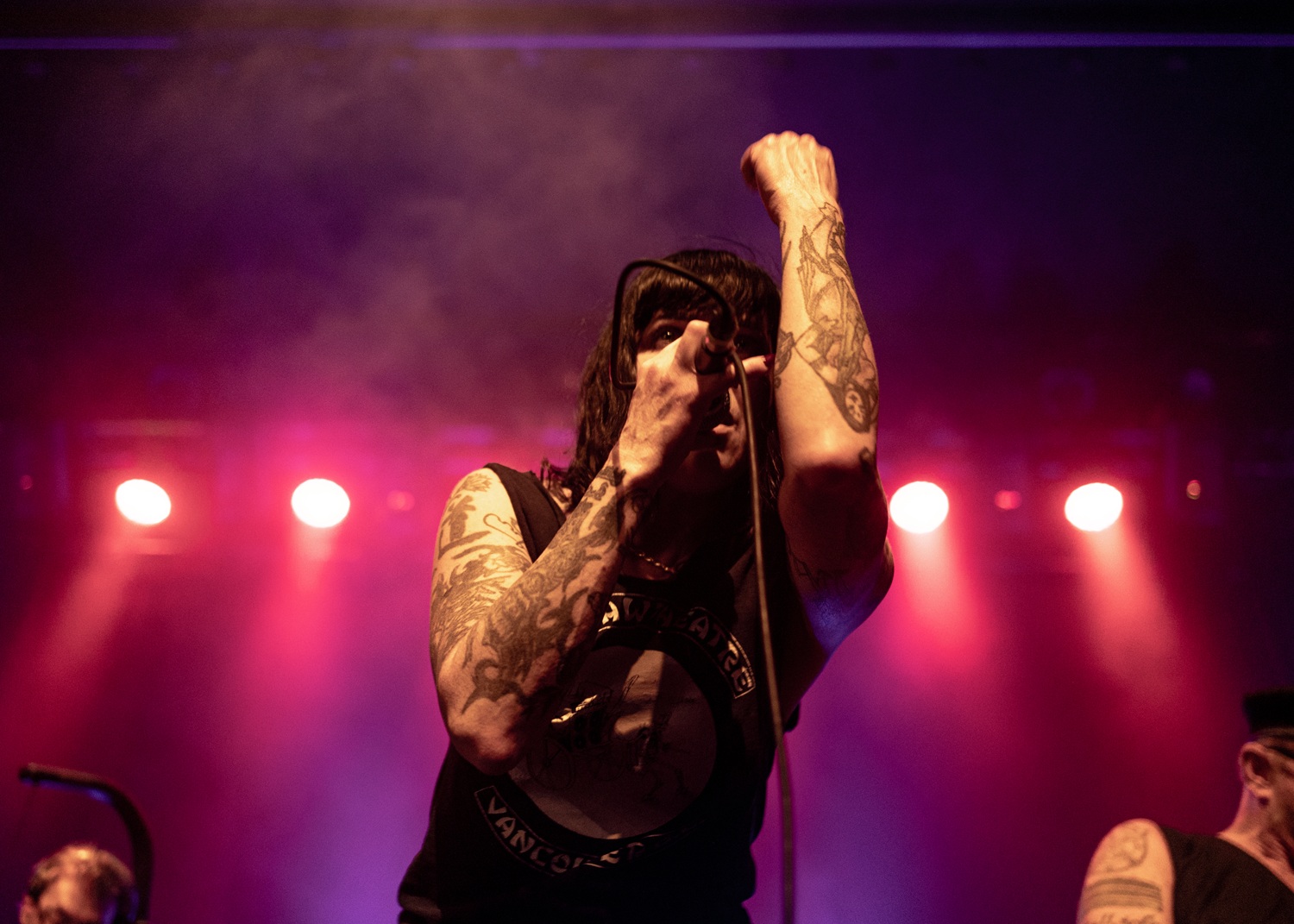 Bif Naked sings on stage with her fist in the air and coloured spotlights behind her.